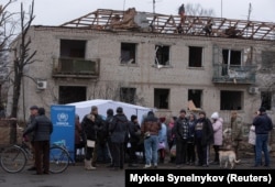 Жители стоят перед домом, поврежденным в результате обстрела в поселке Царичанка Днепропетровской области, 1 декабря 2024 года